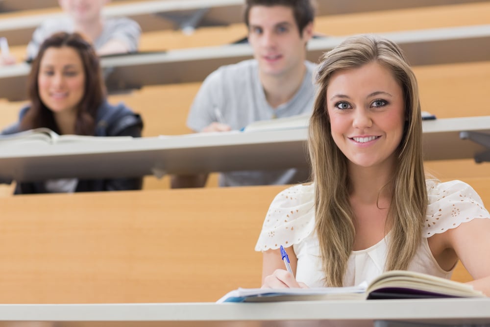 Students sitting at the lecture hall while smiling and taking notes
